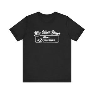 May include: Black t-shirt featuring the white text: "My Other Shirt Gives +2 Charisma." The text is in a playful, slightly vintage font. This is a casual wear item.