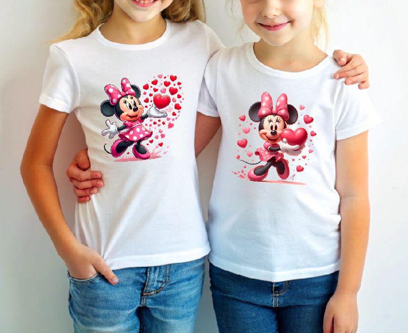May include: Two white t-shirts featuring a Minnie Mouse graphic. The cartoon character is wearing a pink polka-dot dress and bow, holding a heart. Red hearts surround the character. The shirts are paired with blue jeans.