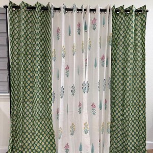 Peut inclure: Un ensemble de trois rideaux à motifs. Deux rideaux verts avec un motif floral répétitif encadrent un rideau blanc avec des motifs floraux et de feuilles colorés. Les rideaux sont suspendus à une tringle noire.