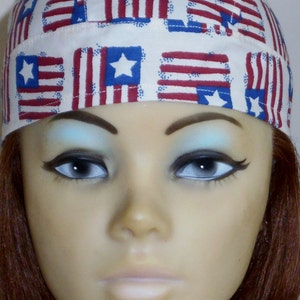 May include: A white bandana with a repeating pattern of red, white, and blue American flags. The bandana is worn on a mannequin's head.