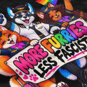 Può includere: Una t-shirt nera con una grafica colorata di tre personaggi animali antropomorfi vestiti da piloti. Reggono uno striscione bianco con il testo MORE FURRIES LESS FASCISTS in lettere in stile graffiti audaci, vivaci e multicolori.