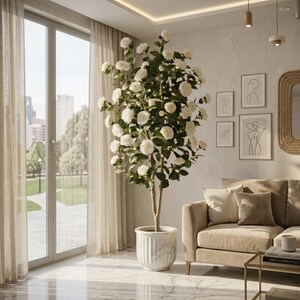 Puede incluir: Un salón con un gran árbol en maceta con flores blancas. El árbol está en una maceta de mármol blanco. Un sofá beige con cojines está cerca. La habitación tiene grandes ventanales y arte abstracto.