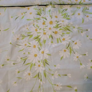 May include: Light blue bedding set with a repeating pattern of white daisies with yellow centers and green leaves. The floral design is arranged in a bouquet style, with some flowers scattered across the fabric. The bedding has a quilted texture.