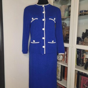 May include: A vintage cobalt blue knit skirt suit. The long-sleeved jacket has white trim, white buttons, and decorative pockets. The matching knee-length skirt completes the two-piece set. The suit is displayed on a black mannequin.