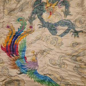 May include: A hand-painted artwork featuring a teal dragon and a colorful phoenix against a cream-colored background. The dragon has yellow accents and a red tongue. The phoenix displays vibrant hues of blue, green, yellow, and red. The artwork includes cloud motifs.
