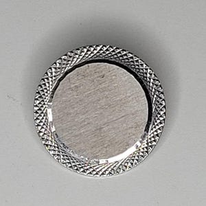 May include: A circular silver-toned button featuring a smooth, brushed metallic center disc surrounded by a textured, diamond-patterned border. The button has a reflective finish and a distinct contrast between the flat inner circle and the rim.