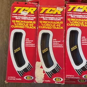 May include: Red boxes of Ideal TCR Total Control Racing curved track. Each box features the text "12 inch radius 1/8 circle-45 curved track" and "Electric HO Scale". The boxes contain 2 curved tracks and have foolproof electro-mechanical connections.