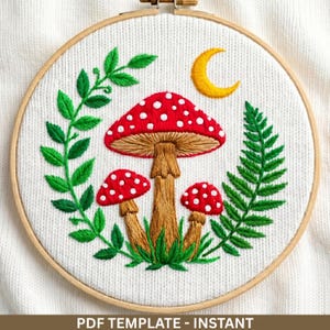 Può includere: Ricamo di un motivo a fungo in un telaio di legno. I funghi hanno cappelli rossi con pois bianchi e gambi marroni, circondati da foglie verdi e una luna crescente gialla. Il testo "PDF TEMPLATE - INSTANT" è in basso.