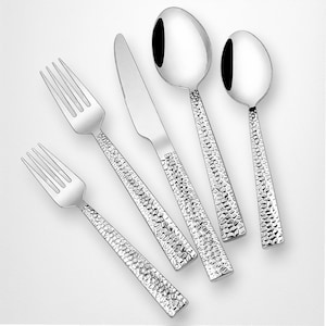 Può includere: Un set di posate in acciaio inossidabile lucido, tra cui due forchette, un coltello e due cucchiai. I manici hanno un design martellato e strutturato. Le posate sono disposte su una superficie bianca.