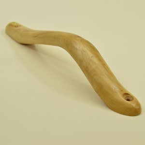 May include: A curved wooden handle with a natural finish. The handle is light brown and has a smooth, organic shape. It features a hole at one end, likely for attachment. The handle is approximately 20 cm long.