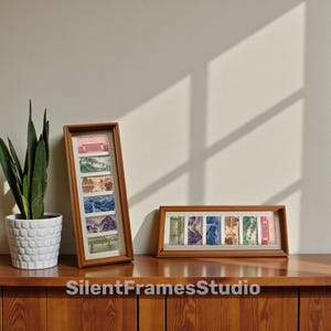 Pode incluir: Duas molduras de madeira com estampas de paisagens. Uma moldura é vertical, a outra horizontal. Estão sobre uma superfície de madeira, com uma planta em vaso à esquerda. O texto "SilentFramesStudio" está na parte inferior.
