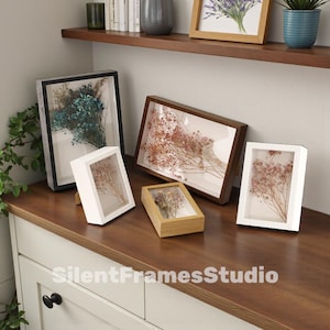 Puede incluir: Una colección de marcos de caja de sombra en varios tamaños y colores, cada uno con flores secas. Los marcos son de madera y tienen una parte delantera de vidrio transparente. El texto "SilentFramesStudio" es visible.