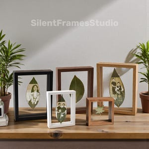 May include: A selection of framed leaf art pieces in different sizes and wood tones. Each frame contains a leaf with a photograph or design. The frames are black, white, and natural wood, displayed on a wooden surface.