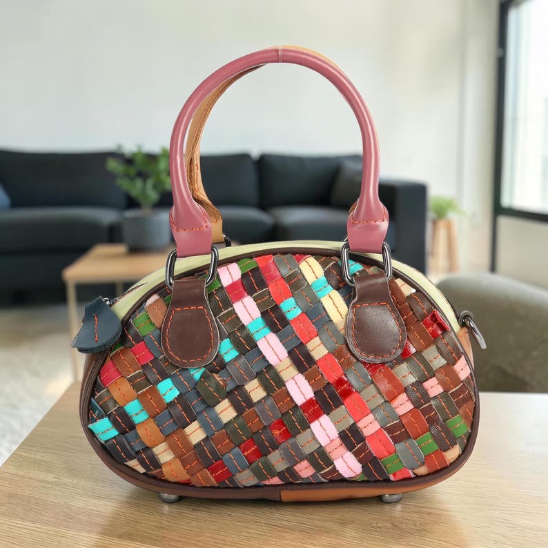 May include: A colorful, woven leather handbag with a rounded shape. The bag features a variety of colors, including red, blue, brown, and pink, in a basketweave pattern. It has a pink handle and brown leather accents. The bag is approximately 9 inches wide.