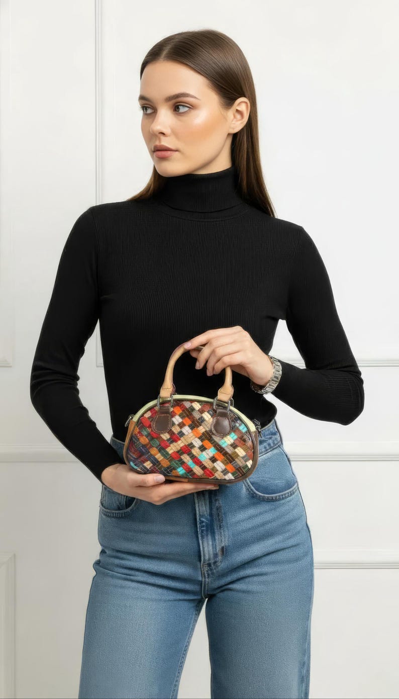 May include: A small, oval-shaped handbag with a woven pattern in various colors, including red, orange, blue, and brown. The bag has a tan handle and brown leather trim. The bag is approximately 8 inches wide.