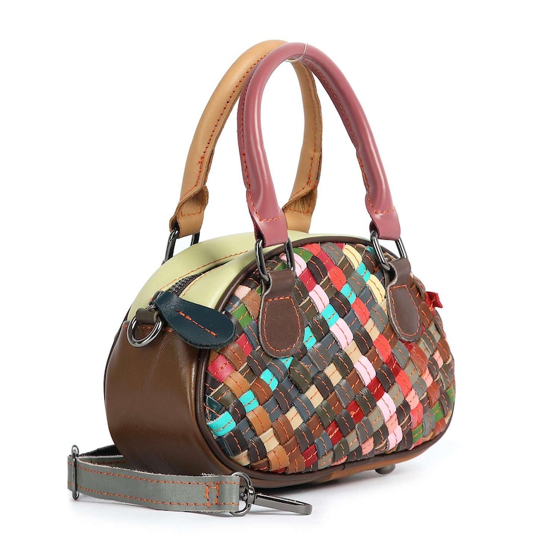 May include: A small, round handbag with a woven, multi-colored design. The bag features a brown leather base, a light green top, and a pink and tan handle. It also has a detachable gray strap.