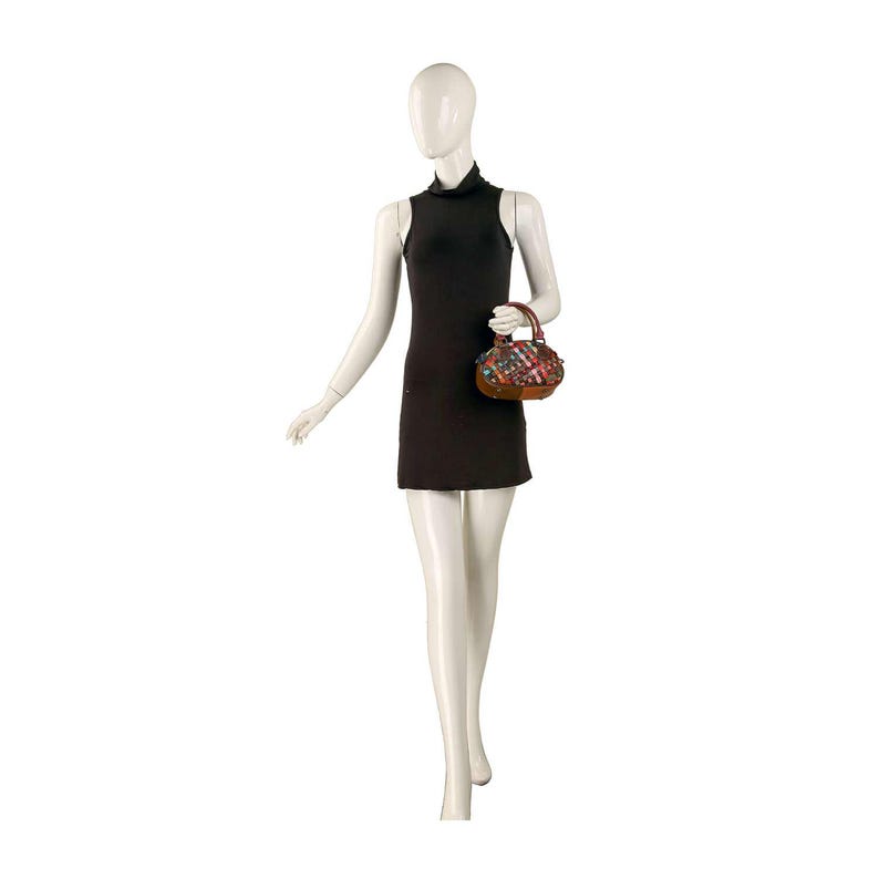 May include: A mannequin wearing a black sleeveless mini dress and carrying a small, colorful handbag. The handbag has a brown handle and is decorated with a patchwork of various colors and patterns. The mannequin is on a white background.