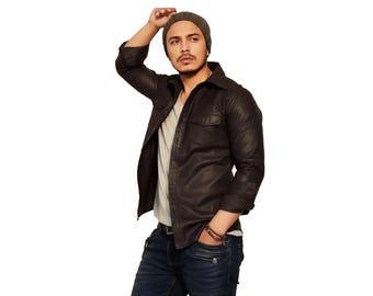 May include: A dark brown button-down shirt with long sleeves and two chest pockets, worn over a light gray t-shirt. The outfit includes dark blue denim jeans, a gray knit beanie, and a beaded bracelet on the wrist, presented against a plain background.