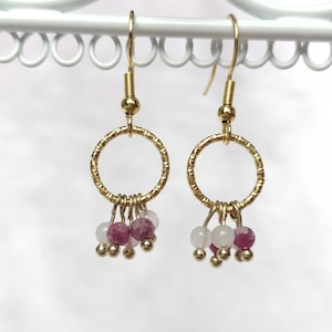 Könnte beinhalten: Ein Paar goldfarbene Creolen mit strukturierter Oberfläche. Jeder Ohrring hat kleine Cluster aus rosa und weißen Edelsteinperlen, die von unten herabhängen. Die Ohrringe werden vor einem weißen Hintergrund präsentiert.