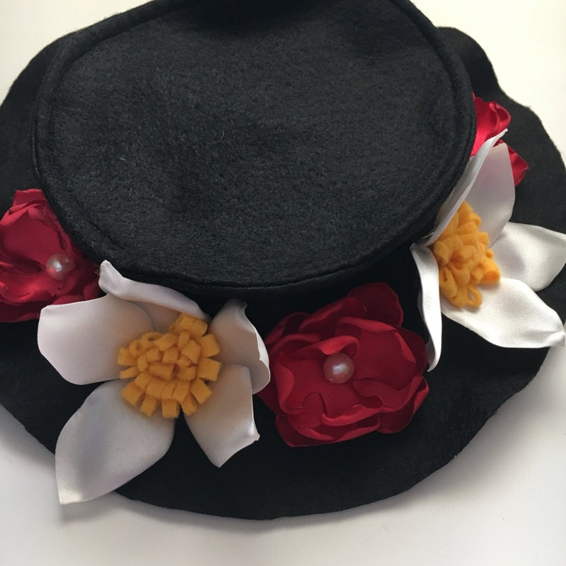 May include: A black felt hat with a wide brim, decorated with white and red felt flowers. The flowers have yellow centers and pearl accents.