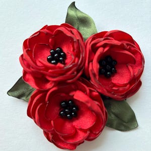May include: Three red fabric flowers with black bead centers and green fabric leaves.