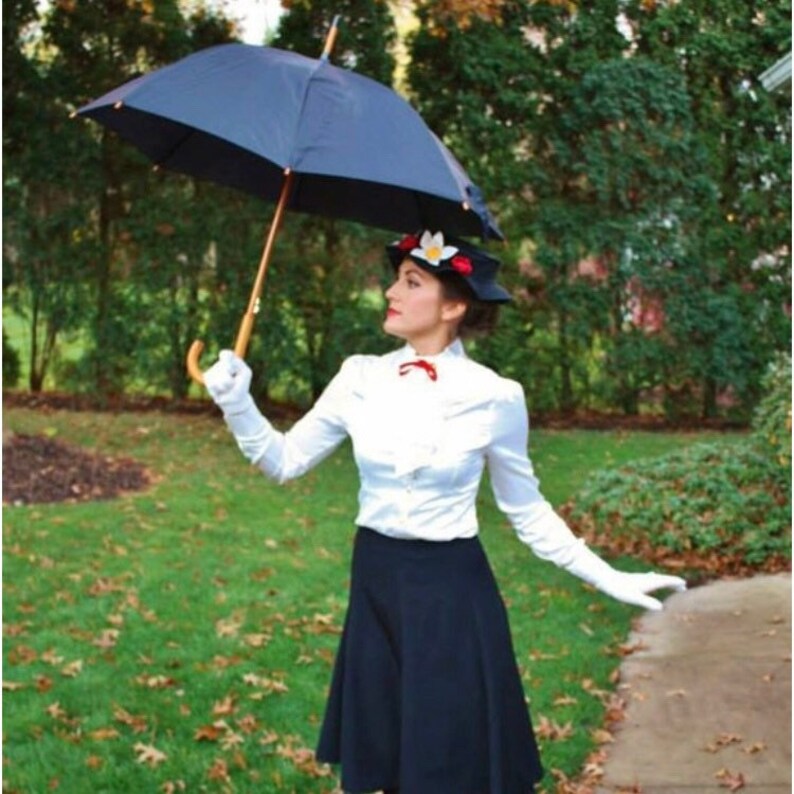 May include: A woman dressed as Mary Poppins, wearing a white blouse with a red bow, a black skirt, and a black hat with white flowers. She is holding a black umbrella.