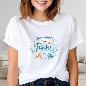 Könnte beinhalten: Weißes T-Shirt mit einem Aquarelldesign. Der deutsche Text "Zu sensibel? Nein. Fische" befindet sich über zwei Fischen. Das Design umfasst einen goldenen und blauen Fisch, Wasserpflanzen und Blasen.