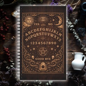 Könnte beinhalten: Ein Spiralnotizbuch mit dunklem Holzmaserungs-Einband. Der Einband zeigt ein detailliertes Ouija-Brett-Design in Gold, einschließlich Buchstaben, Zahlen und Himmelsymbolen. Die Wörter "YES", "NO" und "GOOD BYE" sind ebenfalls sichtbar.