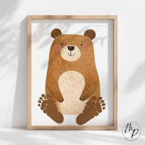 Puede incluir: Una impresión enmarcada con una ilustración de un oso de dibujos animados. El oso es marrón con una barriga beige claro y mejillas rosadas. El oso está sentado con los pies visibles. El marco es de madera clara.