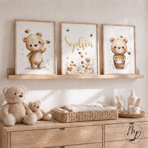 Könnte beinhalten: Drei gerahmte Wandbilder mit Aquarellillustrationen von braunen Bären, Honigbienen und gelben Wildblumen. Der mittlere Druck zeigt den Namen Sophia in goldener Schreibschrift. Die Kunstwerke sind auf einem Holzregal ausgestellt.