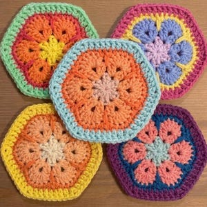 May include: Five handmade crochet coasters in a hexagonal shape. Each coaster features a central floral design with shades of orange, pink, blue, yellow, and green. The coasters are arranged together, showcasing their vibrant colours and intricate patterns.
