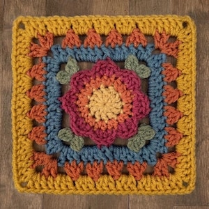 May include: A square, crocheted piece with a floral design. The center features a multi-colored flower in shades of pink, orange, and yellow. The flower is surrounded by blue and orange crochet work, with a yellow border. The piece is likely a decorative item or part of a larger craft project.