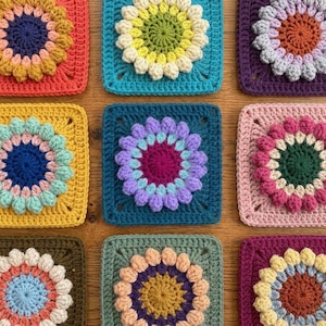 May include: A collection of nine colorful, square crochet pieces. Each square features a central flower design with raised petals in various colors, including orange, blue, yellow, purple, and pink. The squares are arranged in a grid pattern.