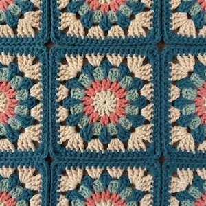 May include: A crochet blanket featuring a repeating pattern of square motifs. Each square consists of a central cream-coloured circle surrounded by layers of dusty pink, sage green, and dark teal yarn, finished with a dark teal square border.