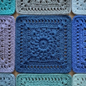 May include: Close-up of a collection of crocheted squares in various shades of blue, teal, and gray. Each square features a unique floral or geometric pattern, showcasing the texture and detail of the handmade craft. The squares are arranged closely together.