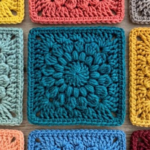 May include: Close-up of several colorful crochet squares in shades of teal, yellow, coral, and blue. Each square features a unique textured design, with a central floral motif. The squares are arranged closely together.