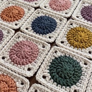 Könnte beinhalten: Nahaufnahme von mehreren gehäkelten Quadraten. Jedes Quadrat hat einen cremefarbenen Rand und einen Mittelkreis in verschiedenen Farben, darunter Rosa, Blau, Orange und Grün. Die Quadrate sind eng aneinander angeordnet und zeigen die handgefertigte Textur.