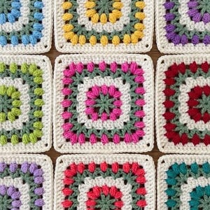 Puede incluir: Una colección de nueve cuadrados de ganchillo coloridos. Cada cuadrado presenta un diseño floral central en varios colores, incluyendo rosa, verde, amarillo y azul, rodeado por un borde blanco. Los cuadrados están dispuestos en un patrón de cuadrícula.