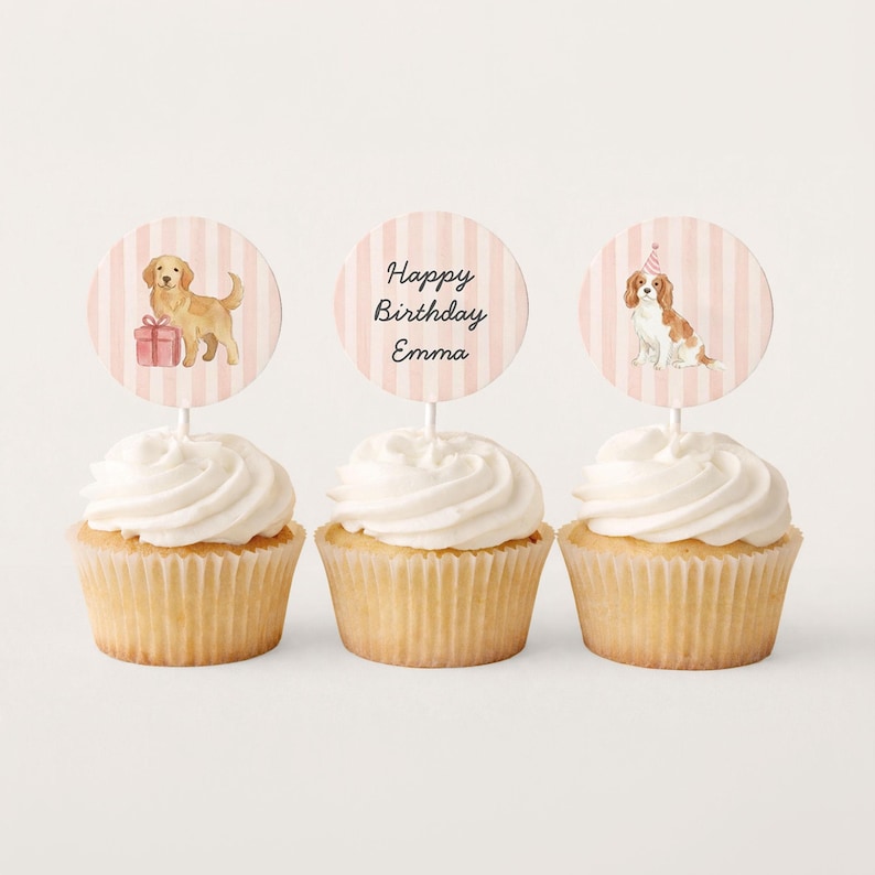 May include: Three cupcakes with white frosting and decorative toppers. The toppers feature a golden retriever with a gift, the text "Happy Birthday Emma", and a Cavalier King Charles Spaniel wearing a party hat.