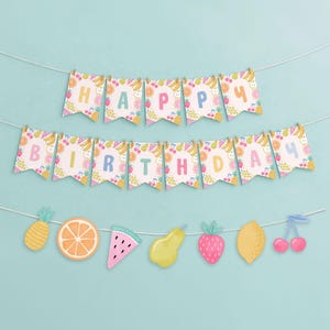May include: A festive birthday banner with the words "HAPPY BIRTHDAY" spelled out on colorful pennants. The pennants are decorated with various fruits, and a string of fruit cutouts hangs below, including a pineapple, orange slice, and watermelon.
