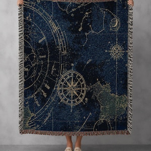 Peut inclure: Un plaid tissé présentant un fond bleu foncé avec des cartes célestes, des constellations et une rose des vents dorée au centre. La couverture rectangulaire possède des bords à franges en haut et en bas, affichant un motif de carte astronomique détaillé avec divers symboles de navigation et formations d'étoiles.