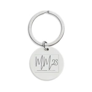 May include: A white, circular keyring with a silver ring. The keyring features the text "MM23" in a handwritten style within a rectangular border. The phrase "MENTAL MOVES" is below the text.