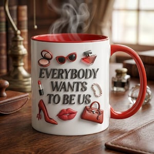 May include: White ceramic mug with a red interior and handle. The mug is decorated with various red and black accessories, including sunglasses, a perfume bottle, and a high heel. The text "EVERYBODY WANTS TO BE US" is displayed on the mug.