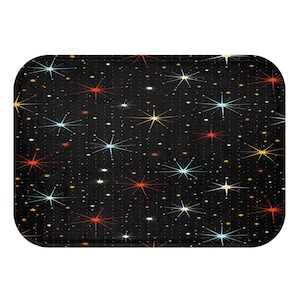 May include: Rectangular black bath mat with a retro starburst pattern in shades of red, yellow, blue, and white. The mat has rounded corners and a dotted background, creating a vintage, space-age aesthetic.