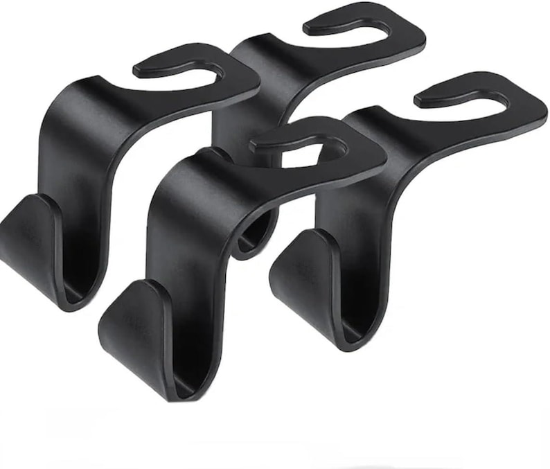 May include: Four black car seat headrest hooks. Each hook has a curved top for hanging and a lower hook for securing items. The hooks are made of a matte black material, designed for car organisation.