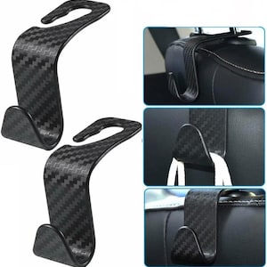 May include: Two black car seat headrest hooks with a carbon fibre pattern. The hooks have a curved design with a hook on each end. Additional images show the hooks in use, hanging from a car seat headrest.