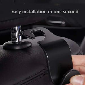 May include: A black car seat headrest hook is being installed. The hook is made of metal and has a curved design. The text "Easy installation in one second" is visible in the image.