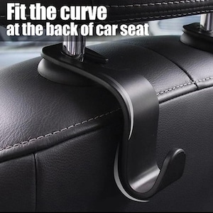 May include: A black car seat hook with the text "Fit the curve at the back of car seat" in white. The hook is designed to attach to the headrest and hang items. The hook is made of a durable material and has a curved design.