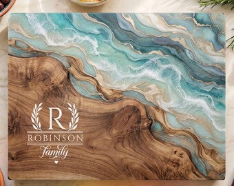Peut inclure: Une planche de service rectangulaire en bois avec une section en grain de bois naturel et une coulée de résine bleue et blanche rappelant des vagues. La planche est gravée avec la lettre R, le texte ROBINSON et le mot Family en écriture cursive.