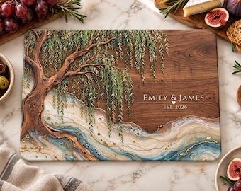 Peut inclure: Une planche à découper rectangulaire en bois ornée d'un saule peint sur la gauche et d'un motif de rivière en résine bleue, blanche et dorée en bas. Le texte EMILY & JAMES et EST. 2026 est imprimé en blanc sur la droite.